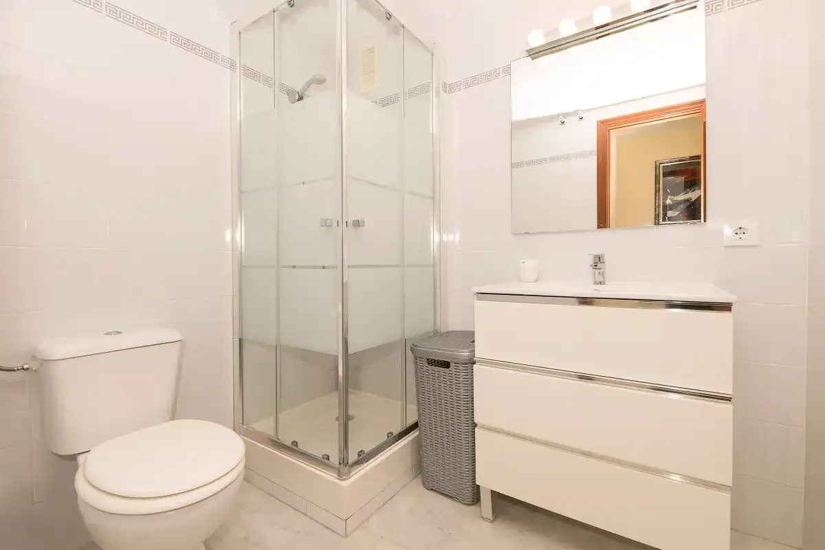 Un baño alicatado cuenta con ducha de vidrio, inodoro y lavabo con espejo.