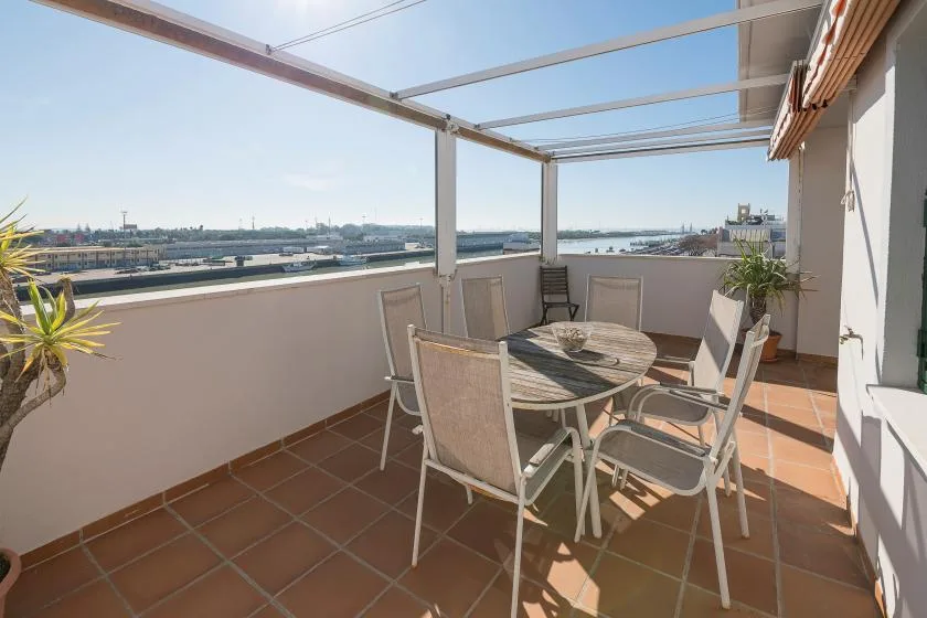 A tiled rooftop terrace has a round table and several chairs beneath a canopy frame.