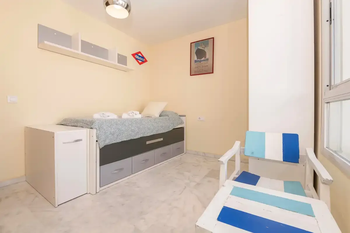 Un dormitorio con una cama individual y una silla de descanso a rayas junto a la ventana.