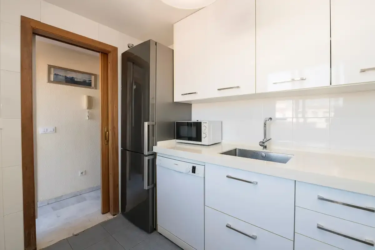 Una cocina luminosa con armarios blancos, encimera y fregadero.