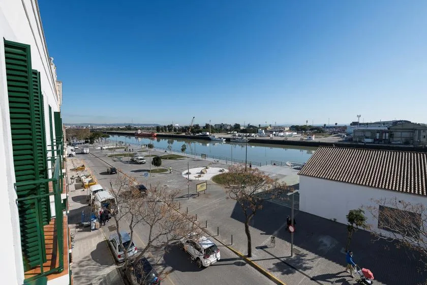 Una calle junto al agua y una zona de estacionamiento dan a un canal amplio bajo un cielo despejado.