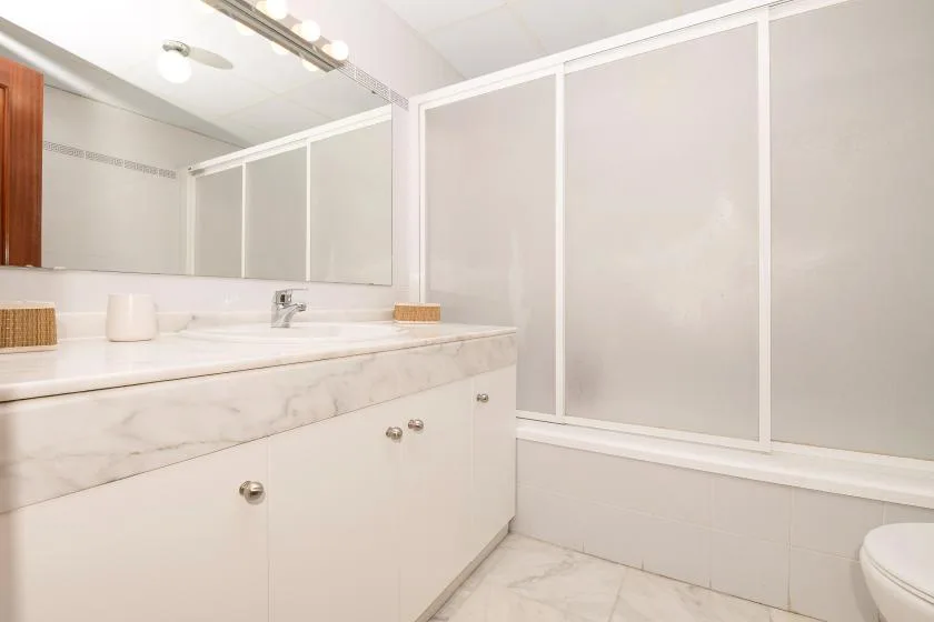 Un baño luminoso con una encimera larga y una ducha de vidrio esmerilado.
