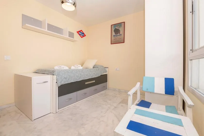 Un dormitorio luminoso con una cama hecha y una silla reclinable a rayas junto a la ventana.