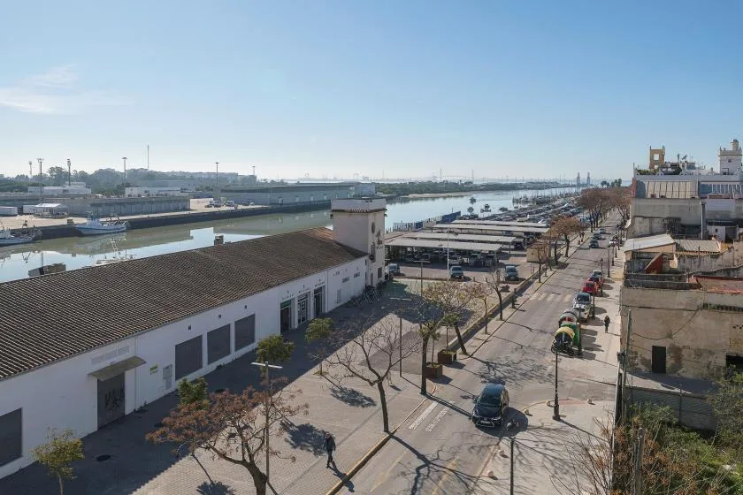 Una calle urbana bordea un canal, con edificios industriales bajos junto al agua.