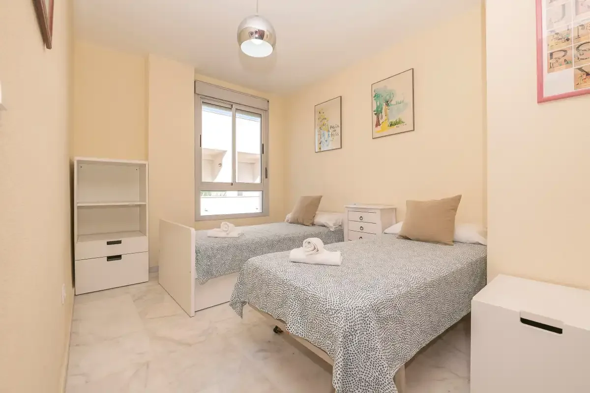 Un dormitorio con dos camas, ropa de cama clara y una ventana.