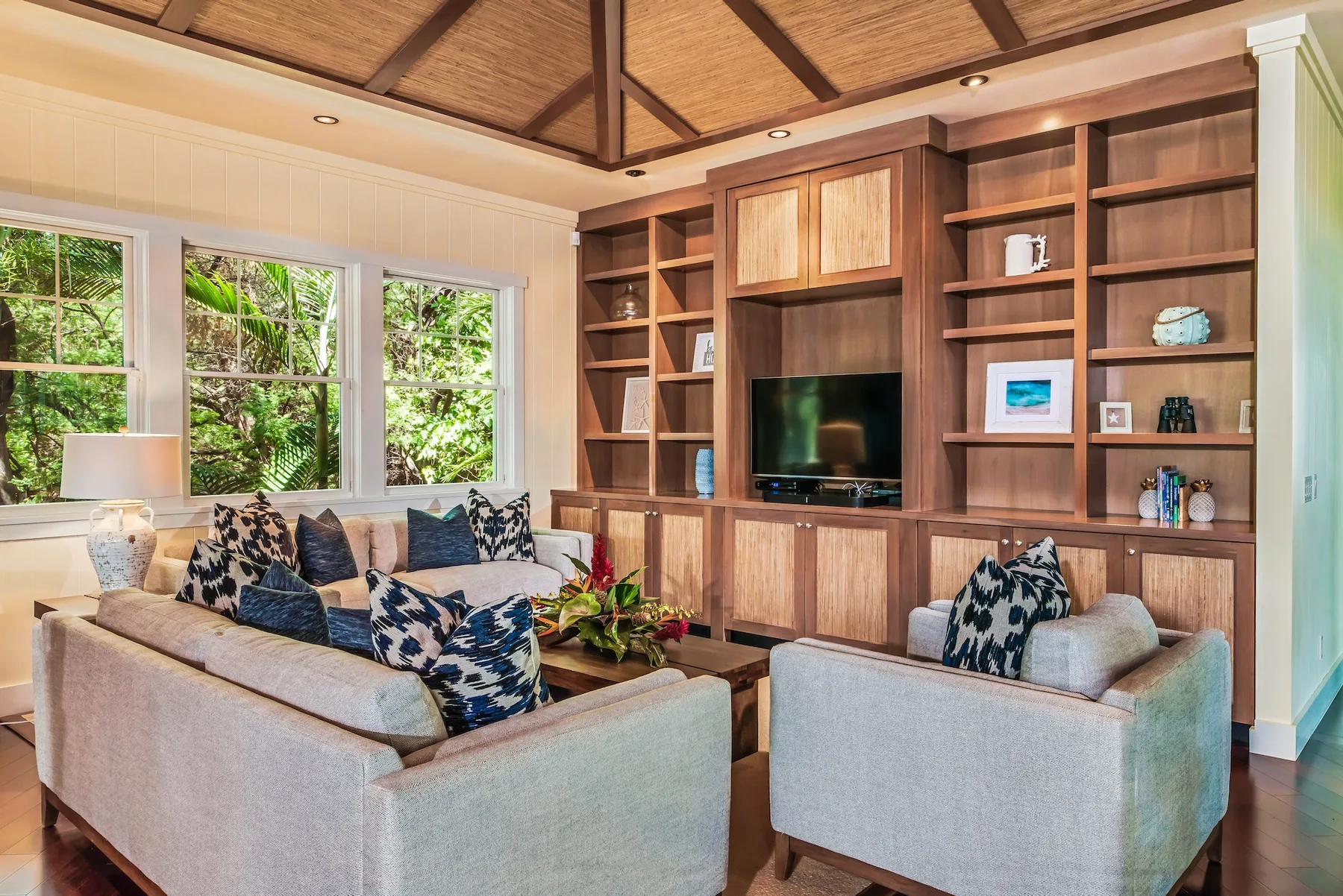 Una sala de estar con asientos alrededor de un televisor y ventanas grandes.