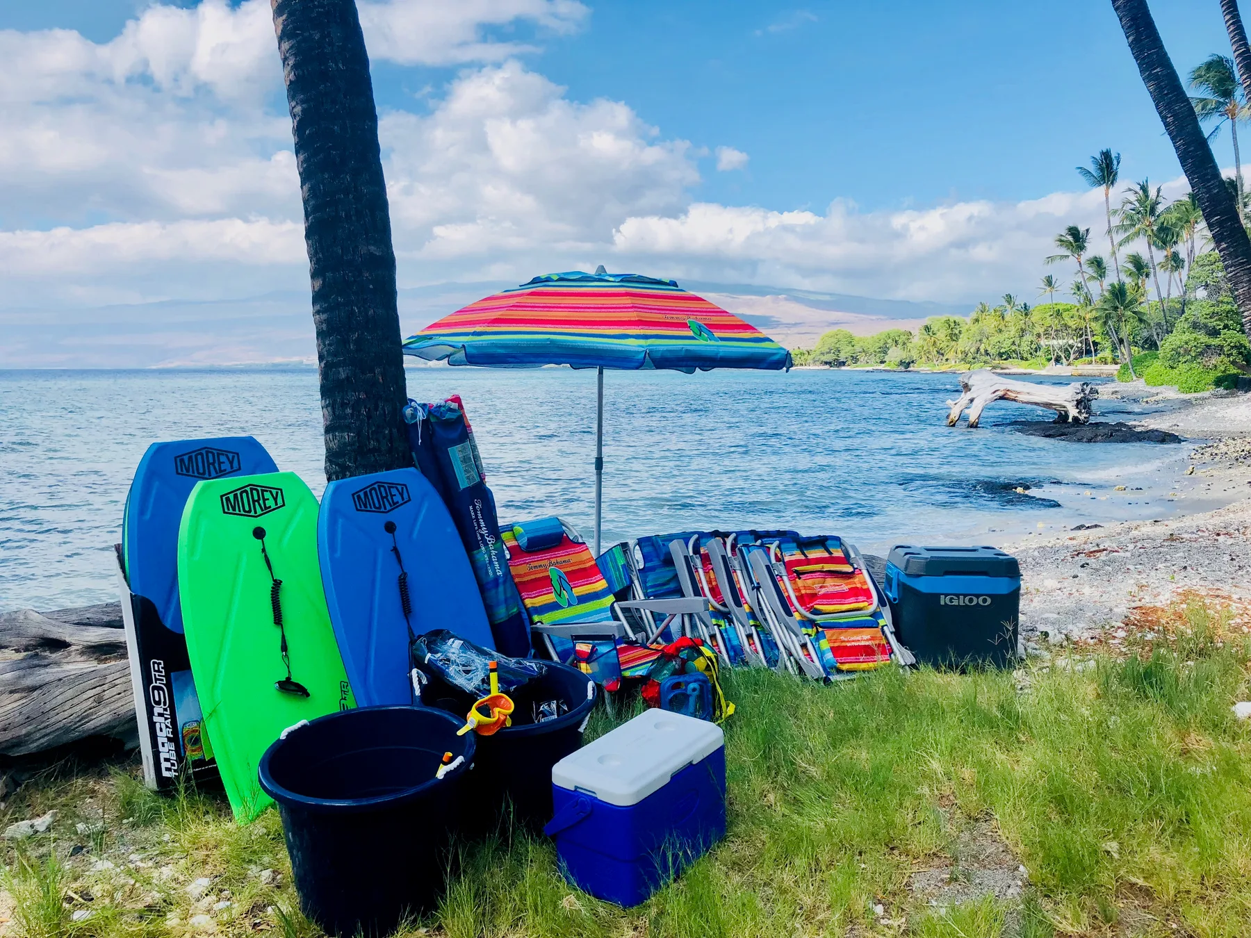 Equipo de playa y sillas coloridas están bajo una sombrilla junto al agua.