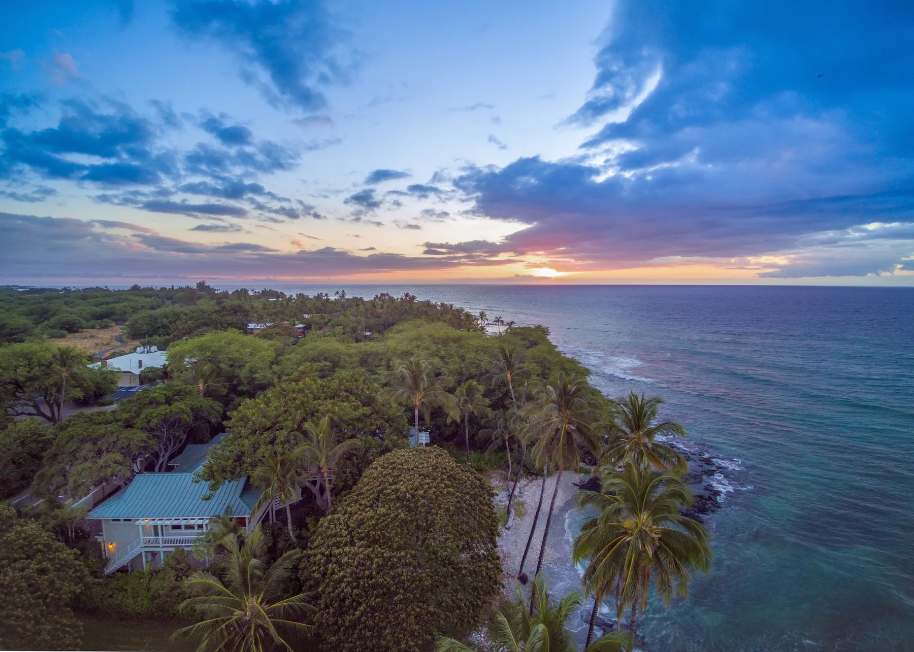 Una costa tropical al atardecer, con palmeras junto al océano.