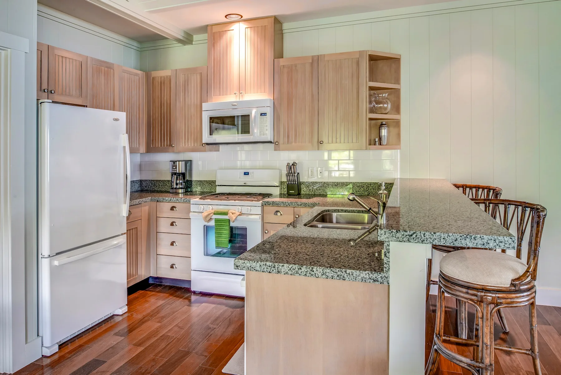 Una cocina con gabinetes de madera clara, un refrigerador blanco y una isla de granito.