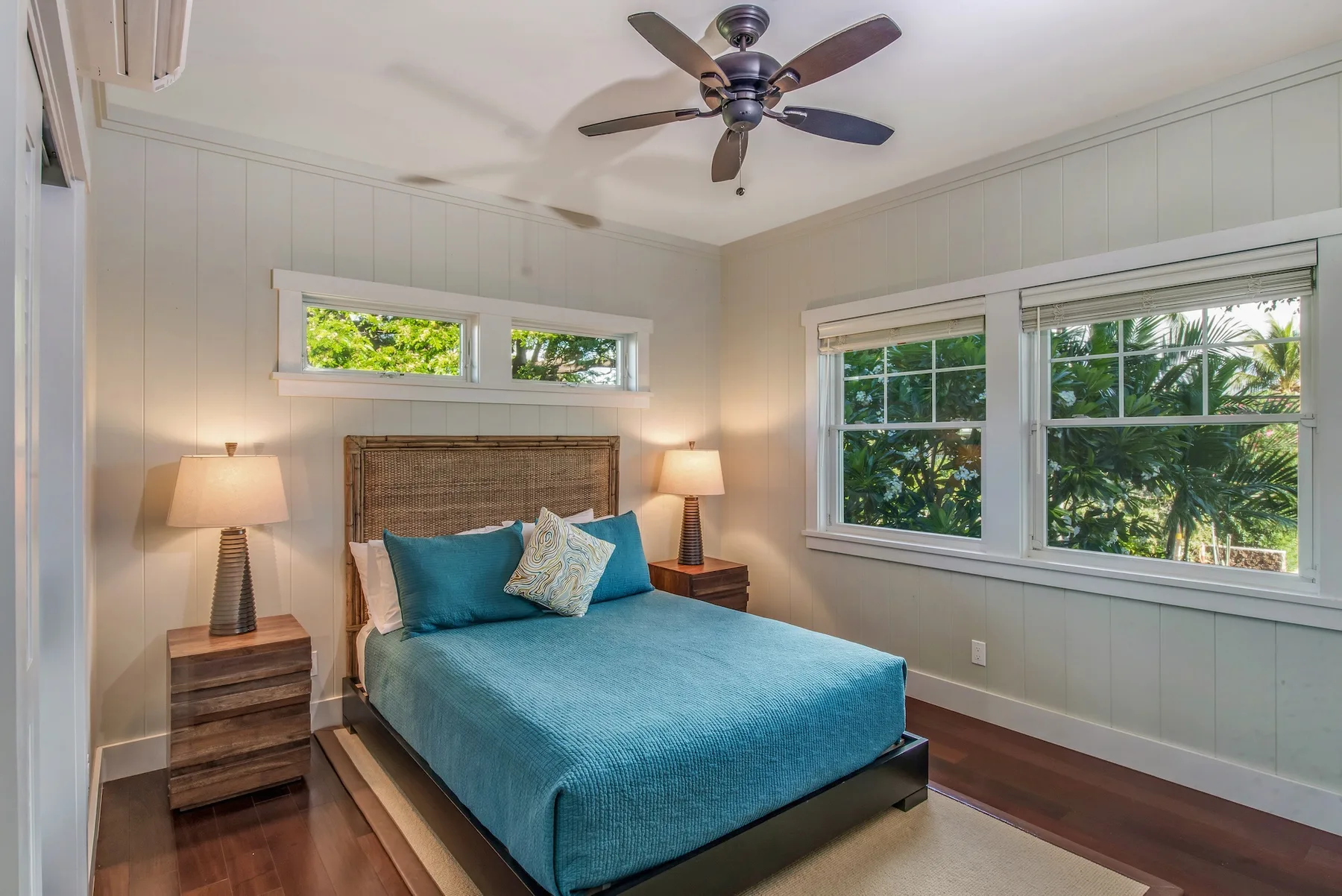 Un dormitorio con una cama vestida de azul y ventanas con vista a la vegetación.