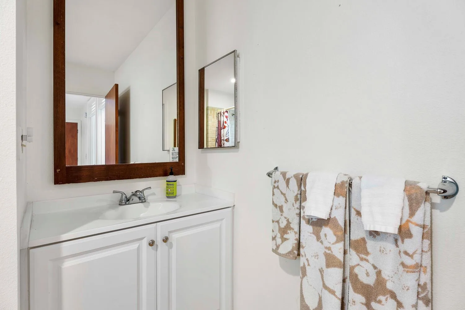 Un tocador de baño con lavabo, espejo y toallas estampadas colgadas en la pared.