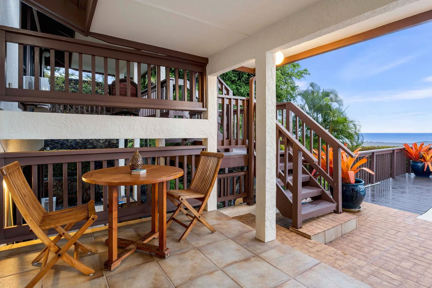 Un patio cubierto tiene una mesa de comedor de madera y escaleras hacia una terraza.