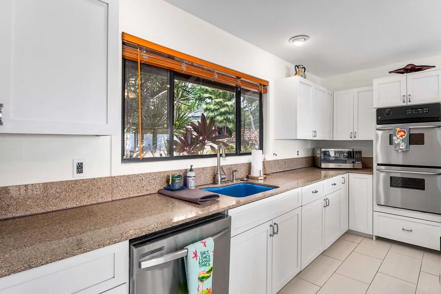 Una cocina luminosa con gabinetes blancos, una encimera larga y una ventana con vista a la vegetación.