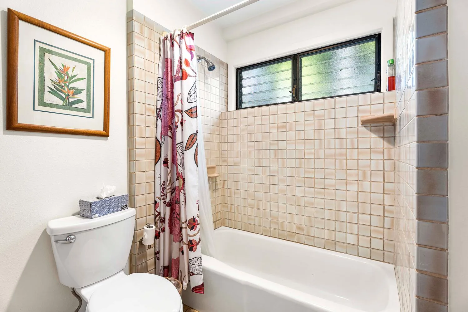 Un baño con azulejos, bañera, ventana y cortina de ducha floral.
