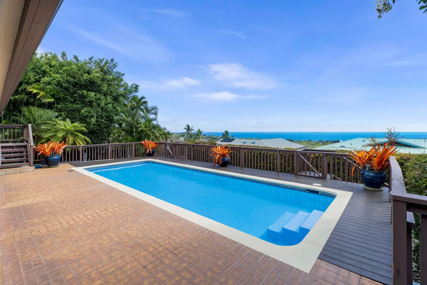 Una piscina al aire libre está junto a una amplia terraza pavimentada, con el océano visible más allá de la barandilla.