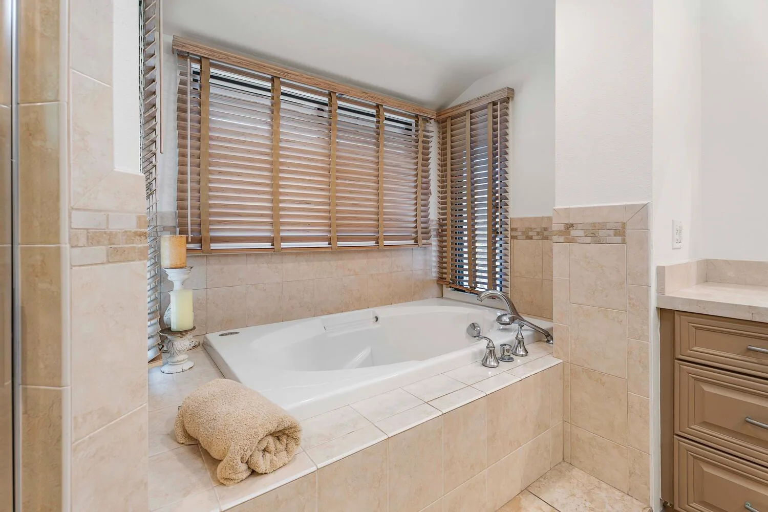 Un baño con una bañera empotrada bajo ventanas con persianas de madera.