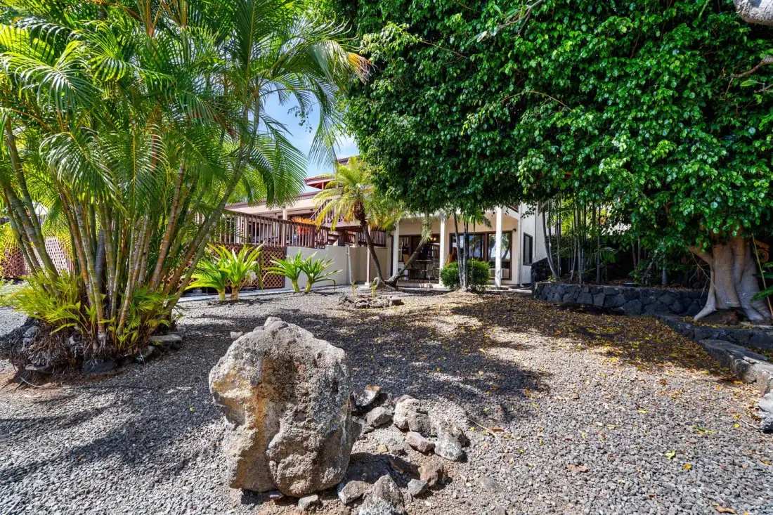 Un jardín tropical con senderos de grava y un patio cubierto entre los árboles.
