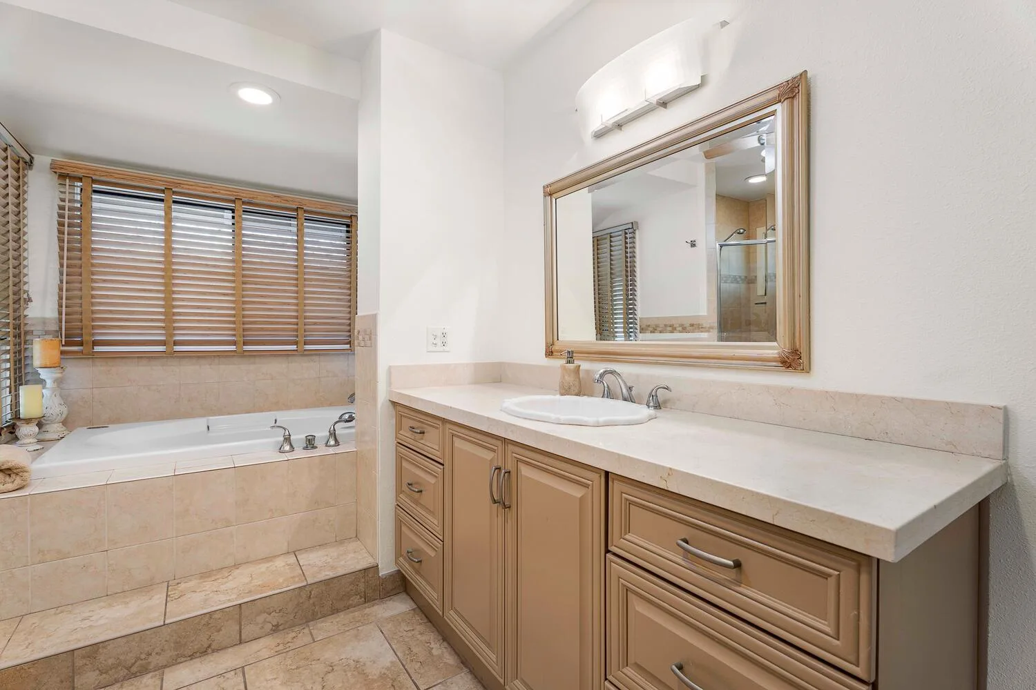 Un baño con bañera bajo una ventana y un largo tocador.