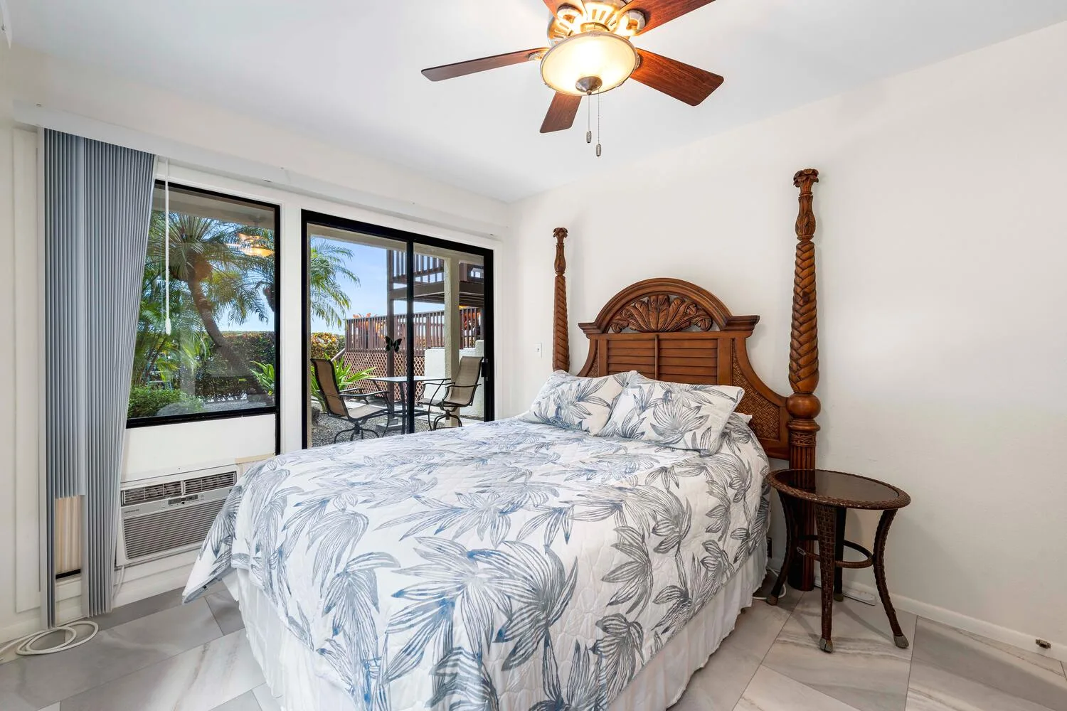 Un dormitorio con una cama vestida con ropa de cama clara estampada junto a grandes ventanas.