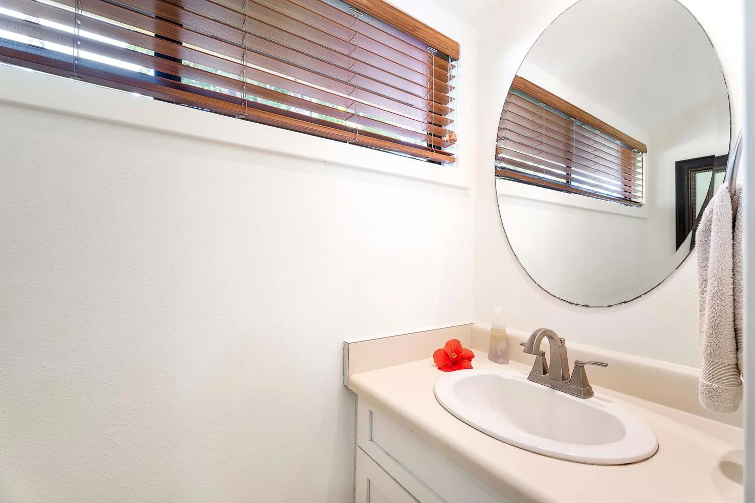 Un tocador de baño con lavabo ovalado, grifo y espejo redondo en la pared.