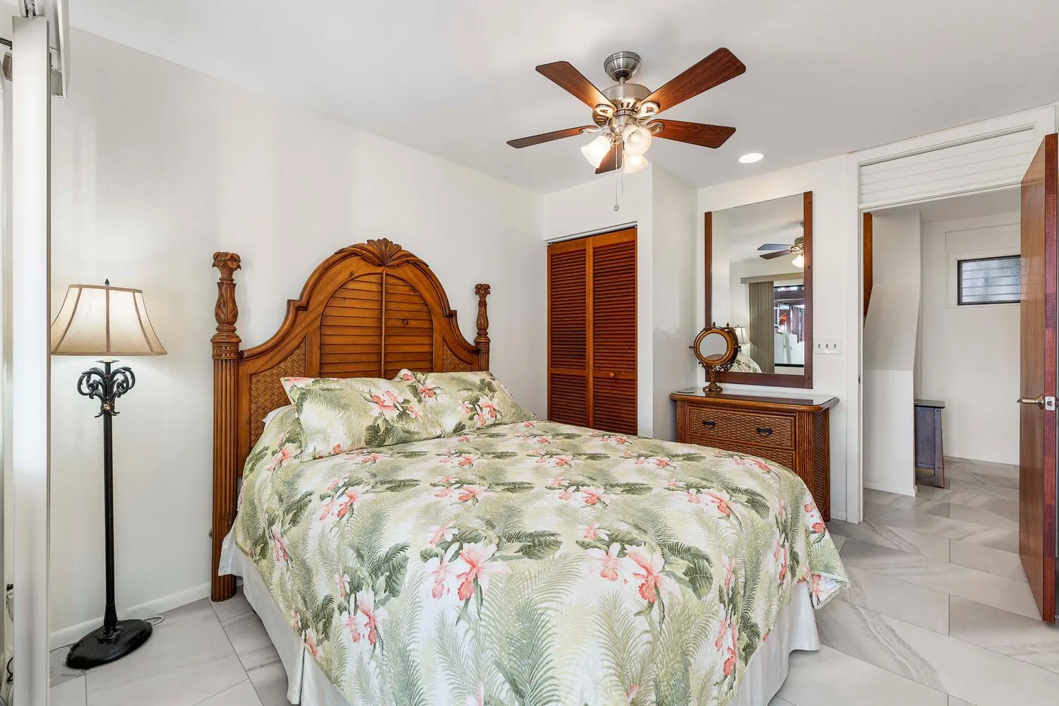 Un dormitorio con una cama cubierta con ropa de cama floral y una cómoda con espejo.