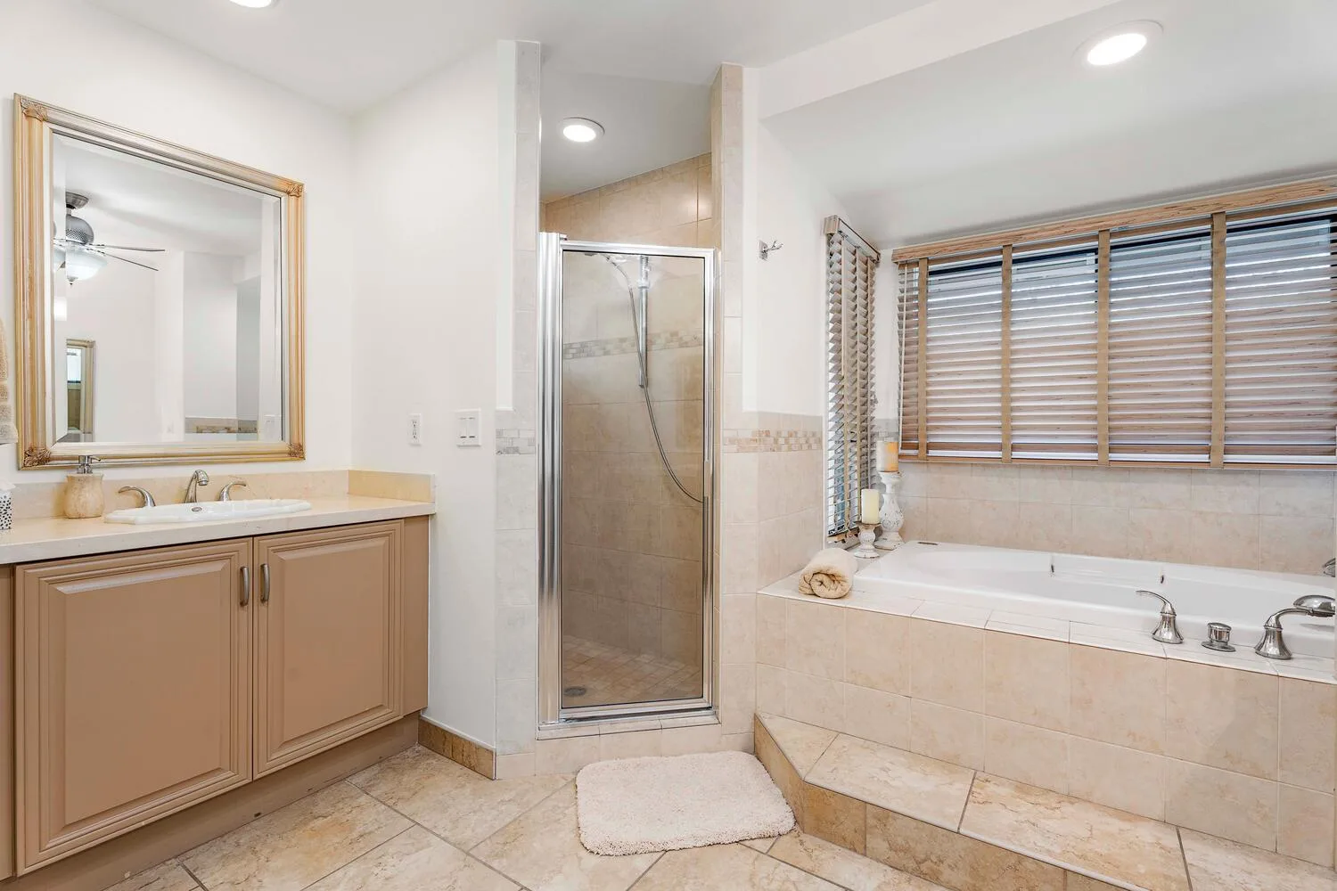 Un baño con lavabo, ducha de vidrio y bañera bajo persianas.