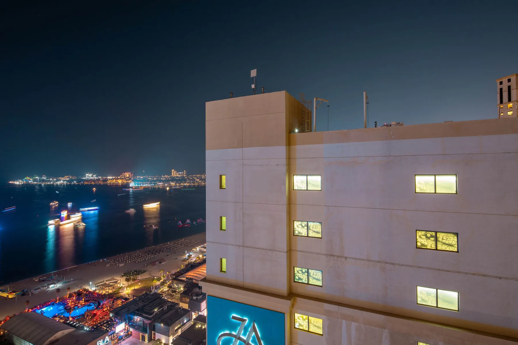 Un edificio moderno da a un paseo marítimo con barcos iluminados y luces de la ciudad por la noche.