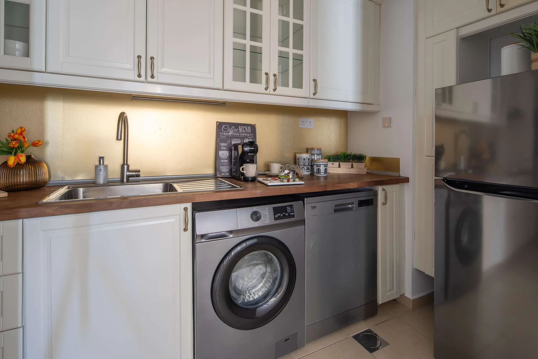 Una cocina luminosa con encimera, fregadero, lavadora y refrigerador.
