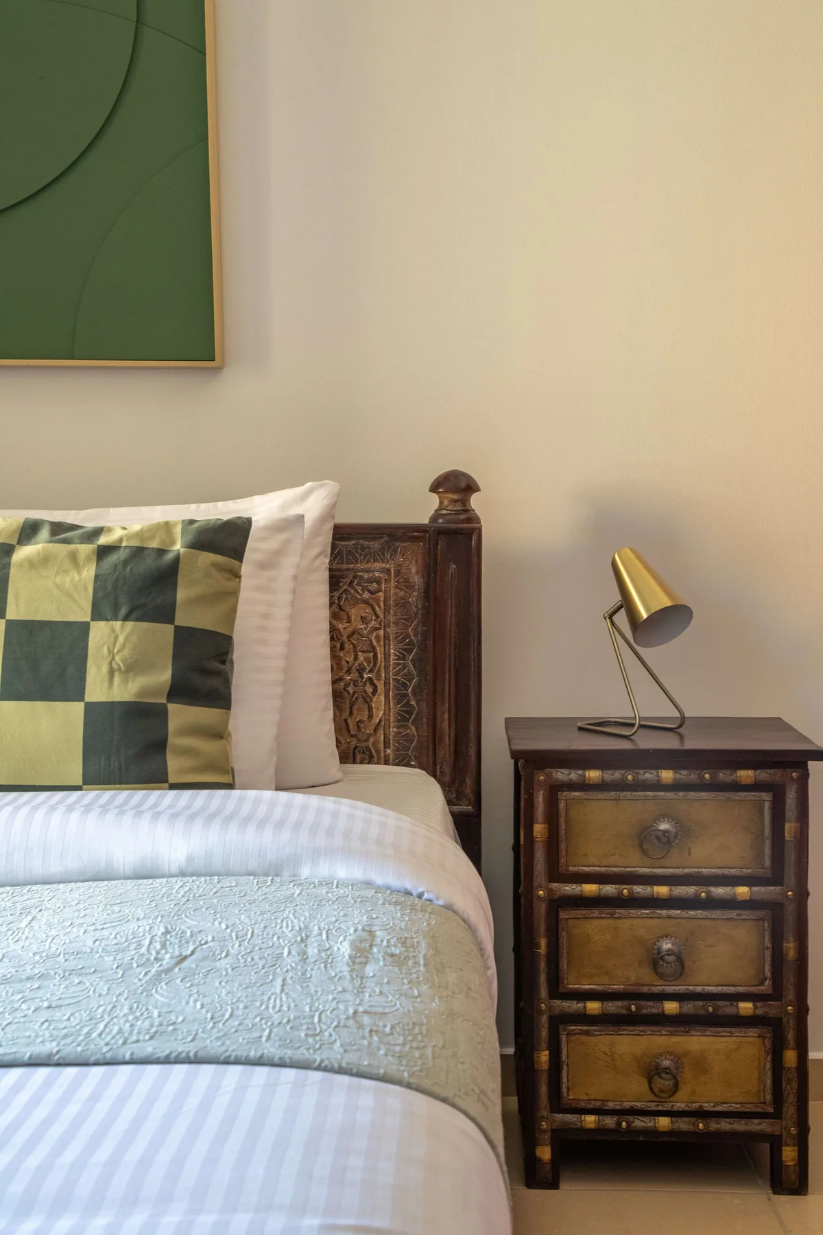 Un dormitorio con una cama junto a una pequeña cómoda y una lámpara.