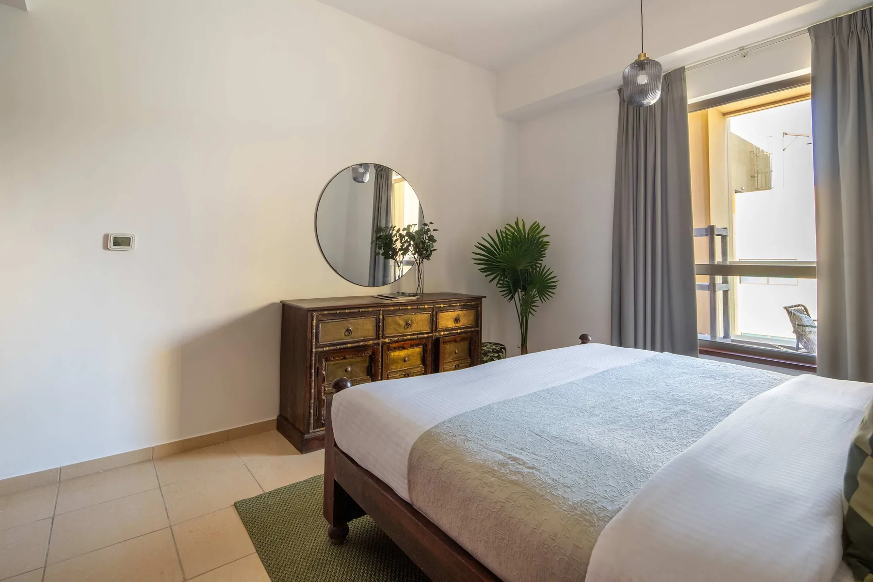 Dormitorio con una cama, una cómoda y una ventana junto a cortinas grises.