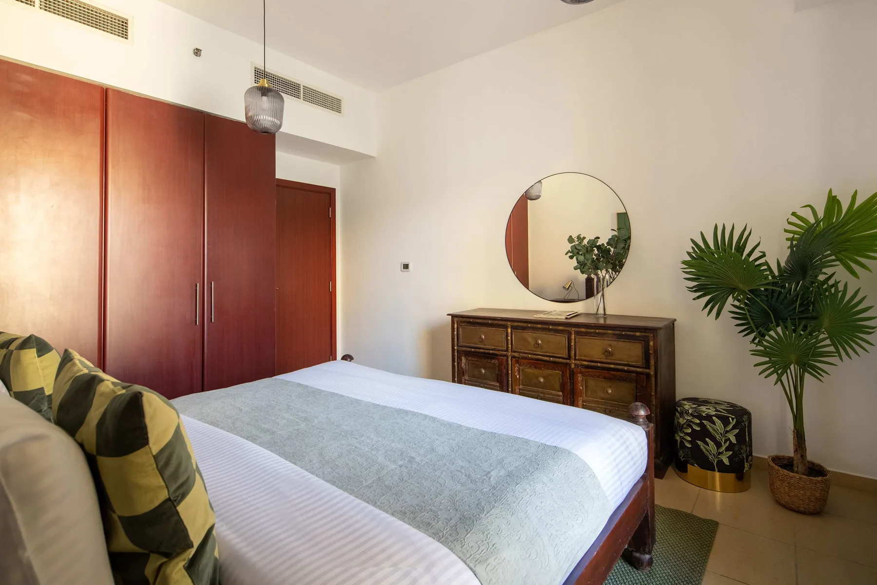 Un dormitorio con una cama, un armario de madera y una cómoda bajo un espejo redondo.