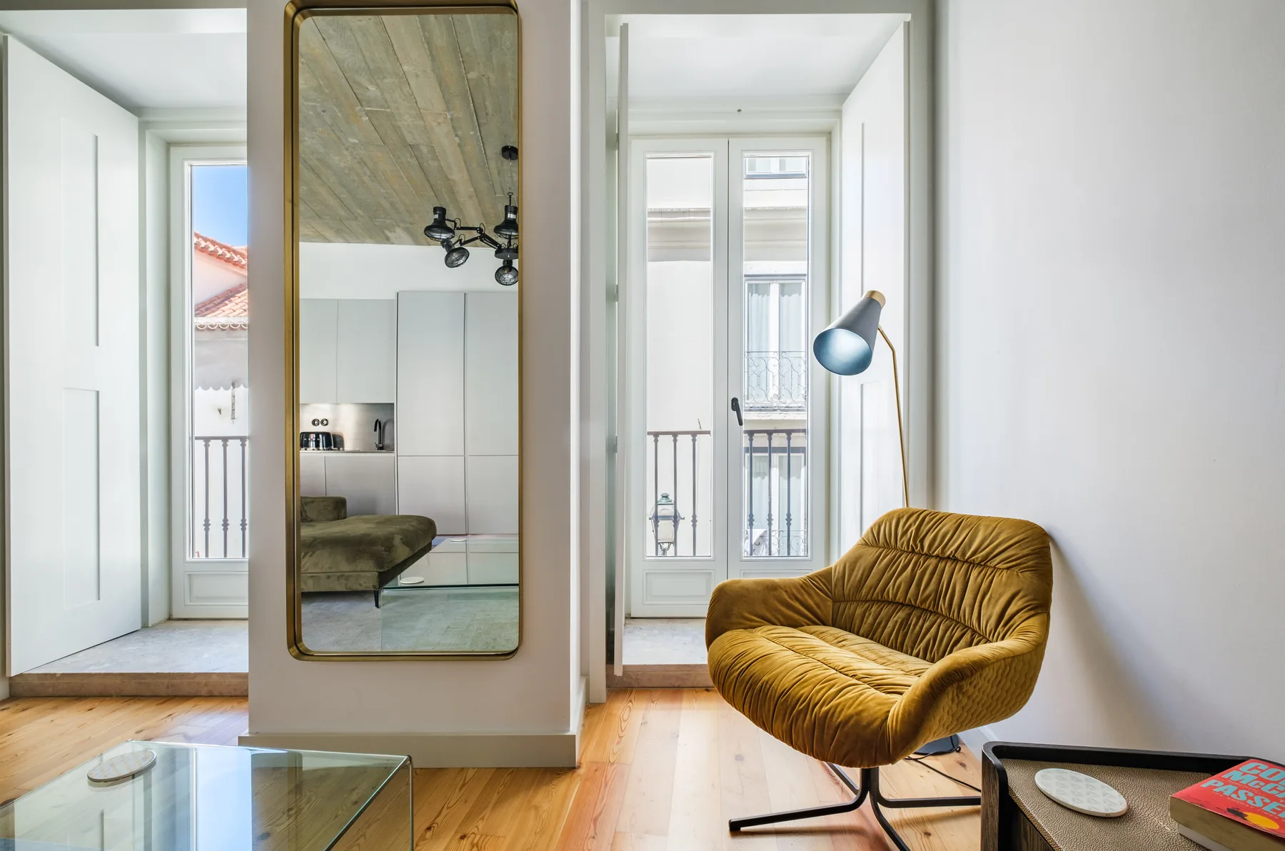 A bright living room with a mustard-colored lounge chair beside tall windows.
