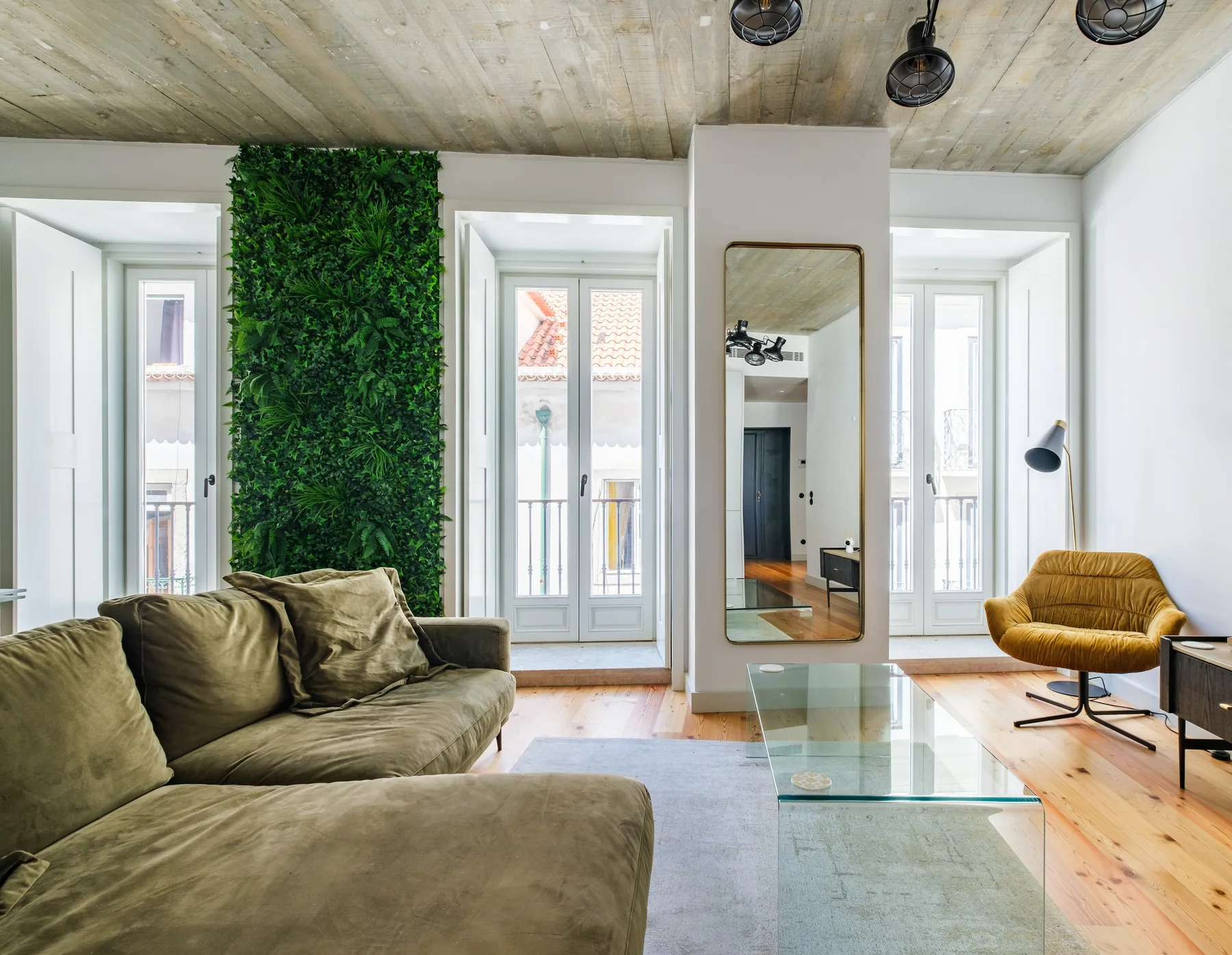 Una sala de estar con un sofá grande, una mesa de centro de vidrio y ventanas altas.