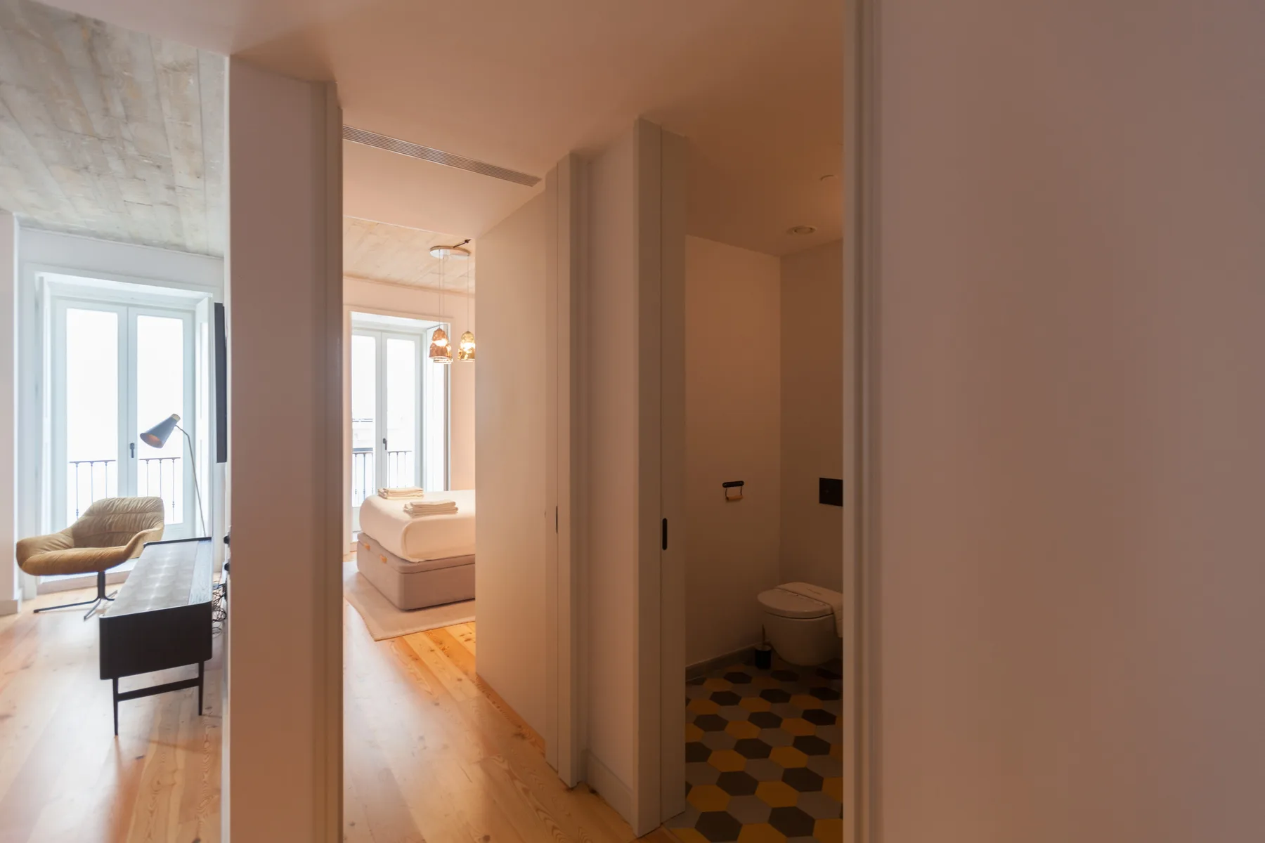 A bright apartment hallway opens onto a bedroom and bathroom.