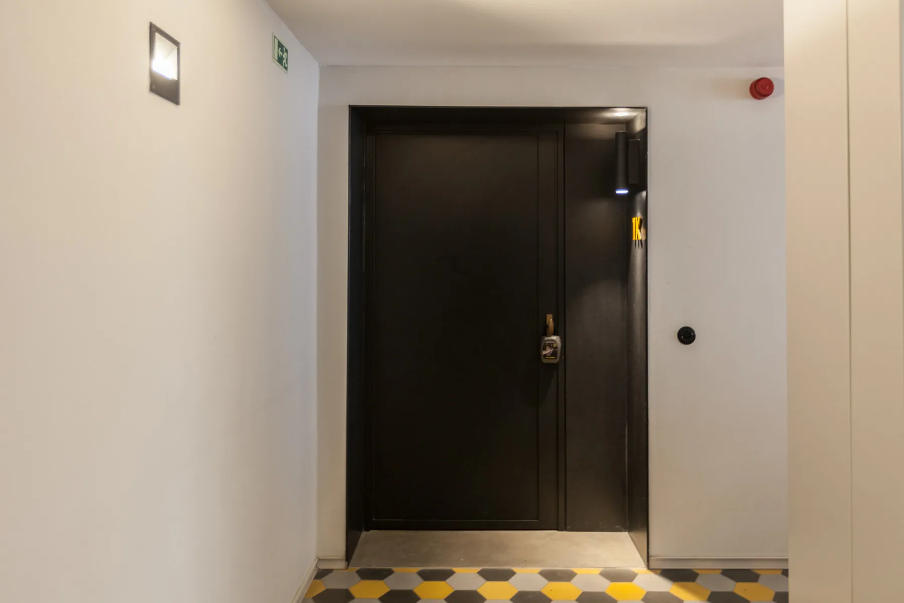 A dark entry door in a bright hallway with patterned floor tiles.