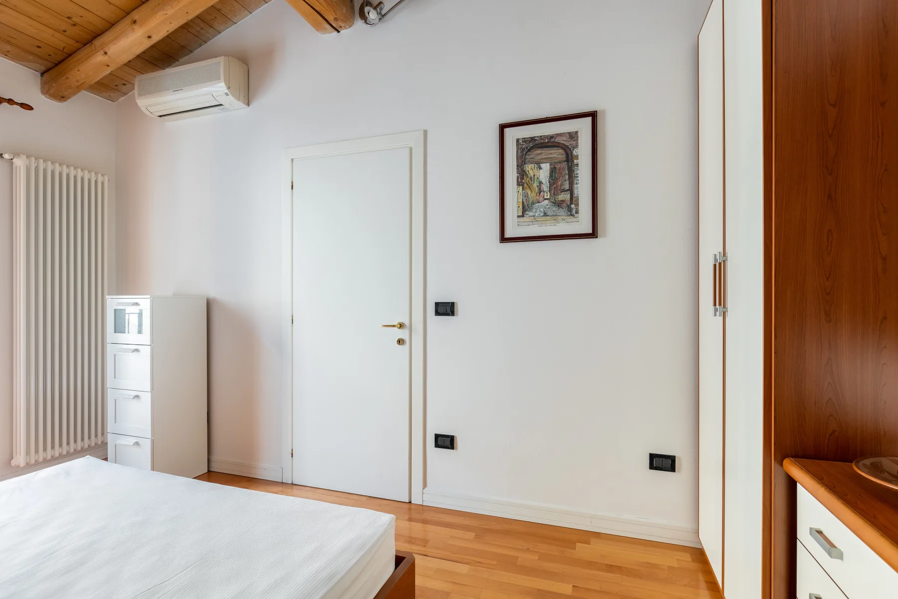 Un dormitorio con una cama, una puerta blanca y un techo inclinado de madera.