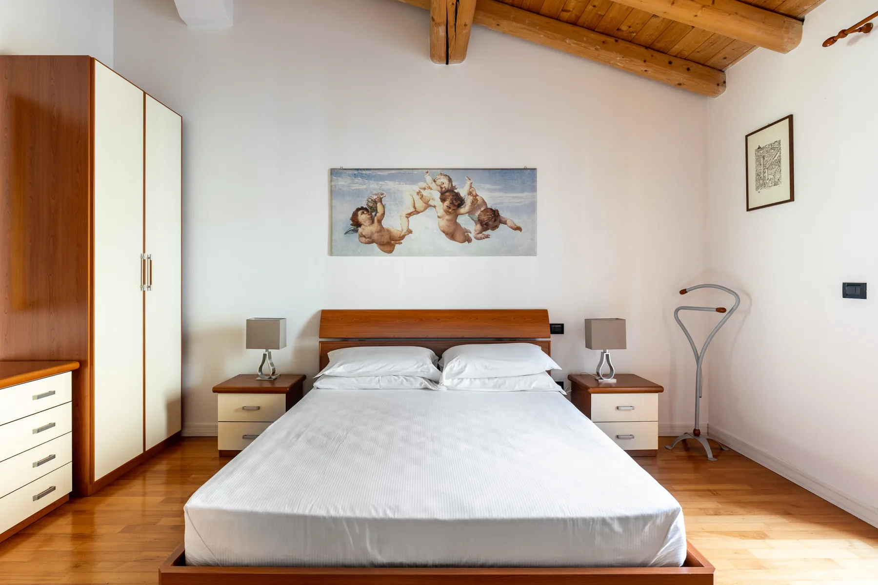 Un dormitorio con una cama bien tendida bajo vigas de madera a la vista.