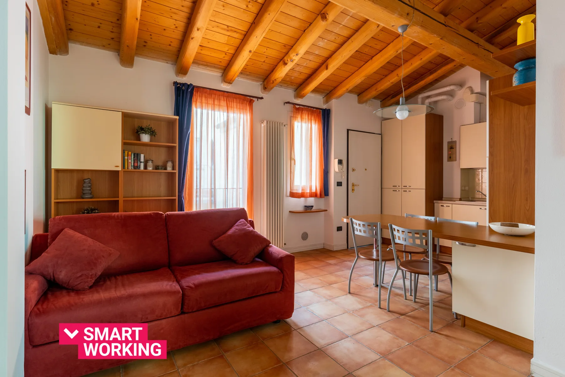 Sala de estar y comedor con asientos rojos, una mesa y vigas de madera a la vista.