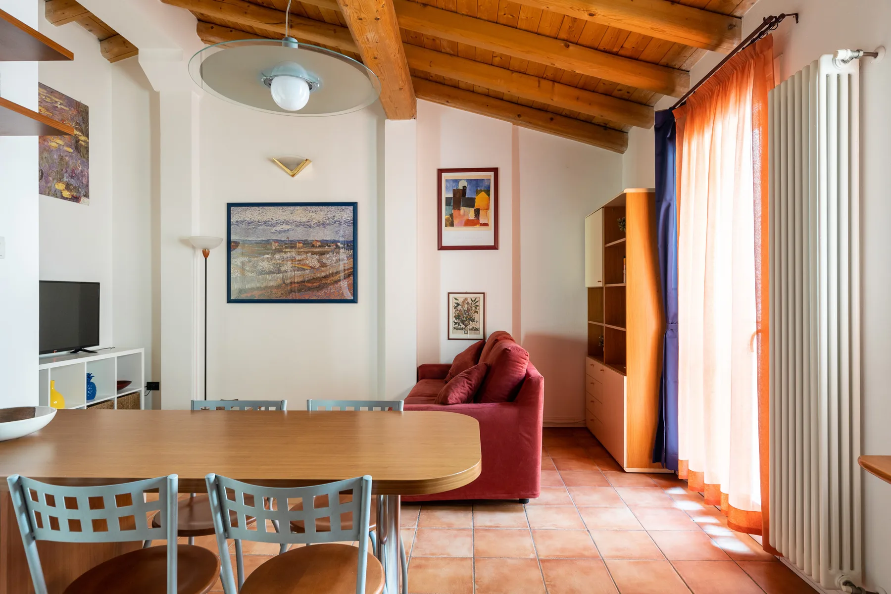 Salón-comedor con un sofá rojo y vigas de madera en el techo.