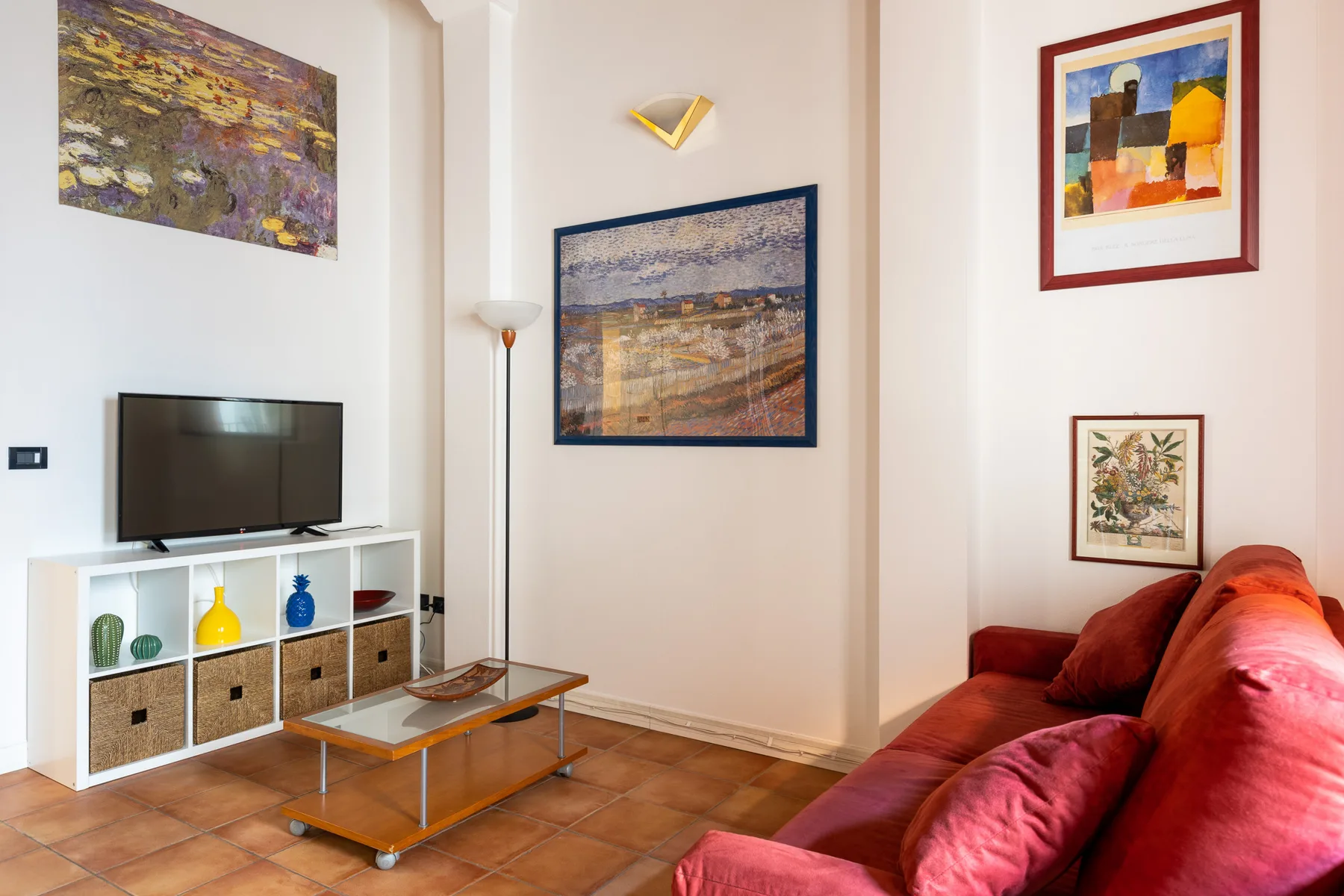 Sala de estar con televisor, cuadros enmarcados y asientos rojos.