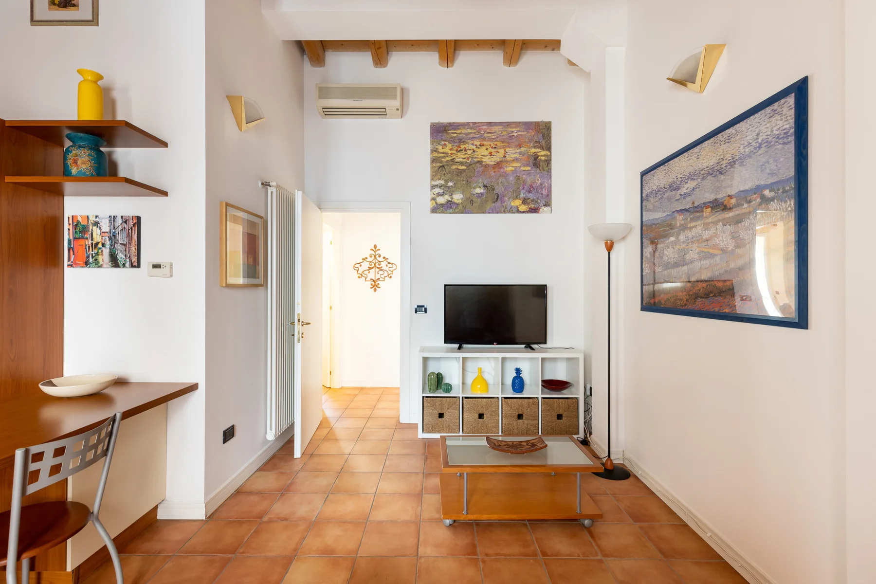 Una sala luminosa con un televisor sobre un mueble bajo y cuadros coloridos.