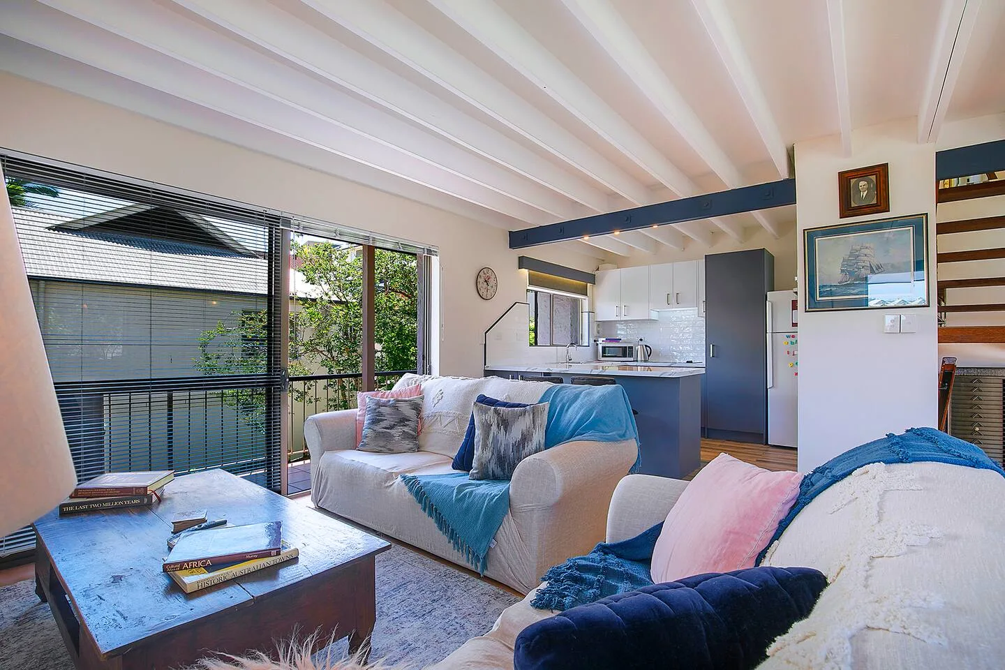 Una sala de estar con asientos junto a grandes ventanas y una cocina abierta.