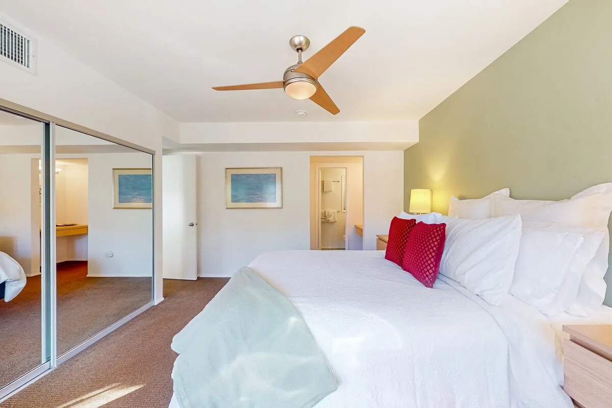 Un dormitorio luminoso con una cama grande, puertas de armario con espejo y un ventilador de techo.