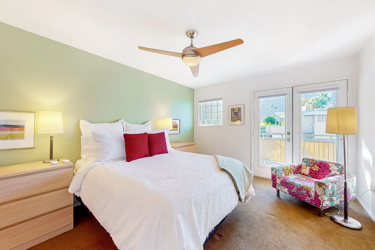 Un dormitorio luminoso con una cama bien tendida y un asiento floral junto a puertas de vidrio.