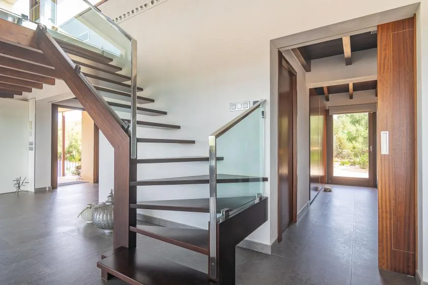 An interior hallway with a staircase and an open doorway to a bright room.