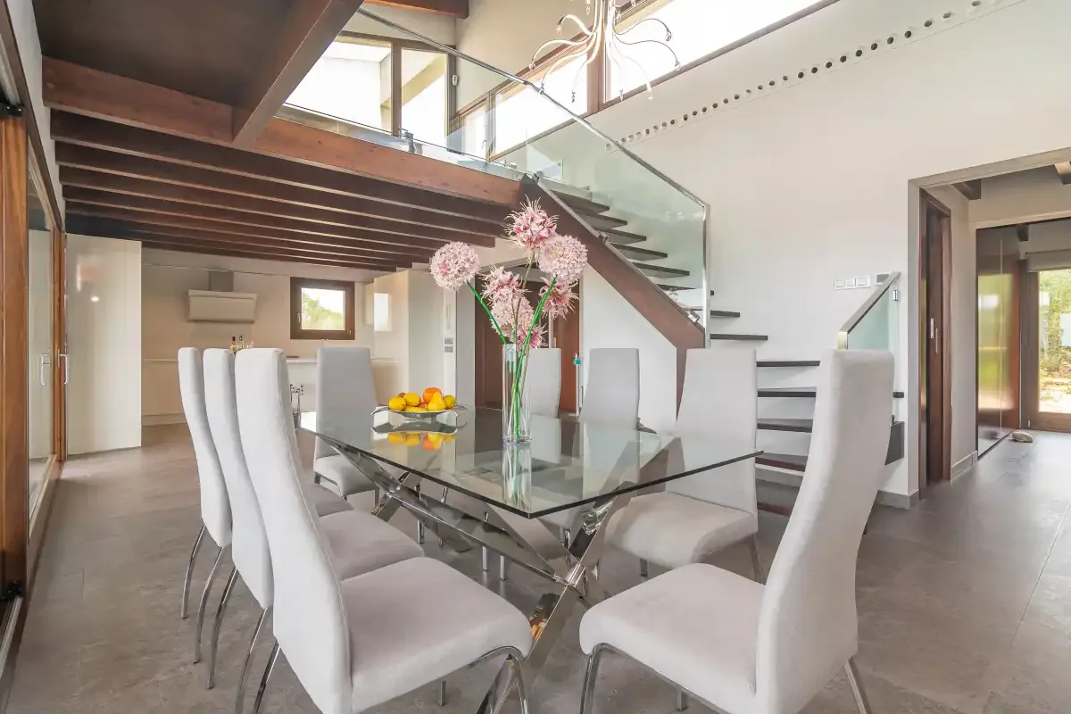 A dining area with upholstered seating and a glass table beneath a staircase.