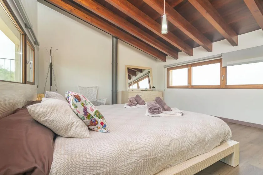 A bedroom with a large bed beneath exposed wooden ceiling beams.