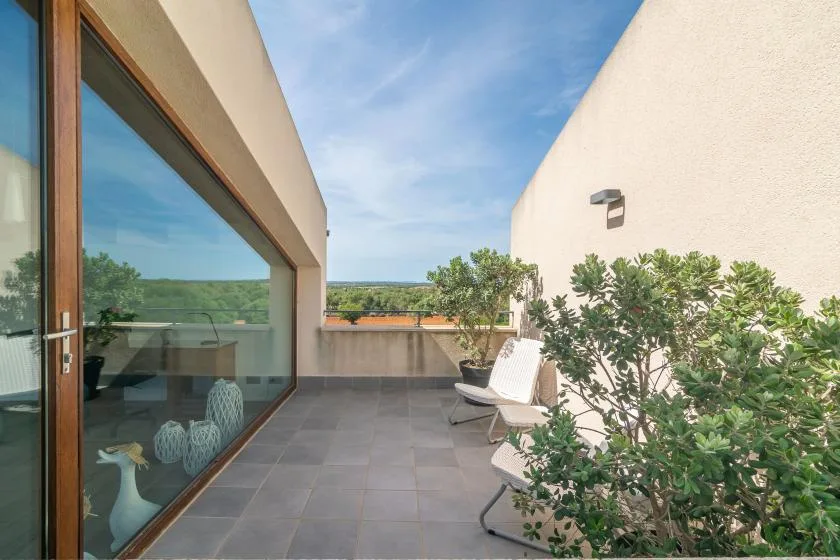 A tiled outdoor terrace has seating beside a glass door and leafy plants.