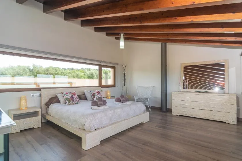 A bedroom with a large bed beneath exposed wooden ceiling beams.