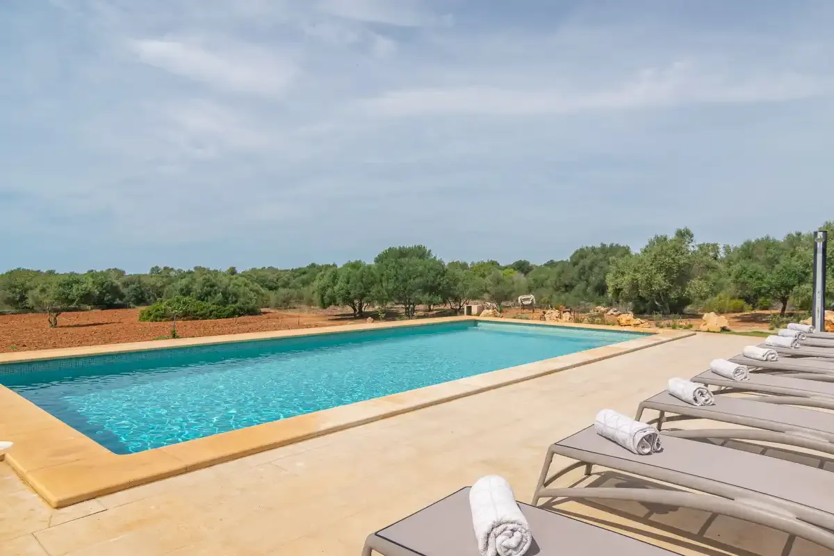 An outdoor swimming pool is surrounded by a spacious paved deck and loungers.